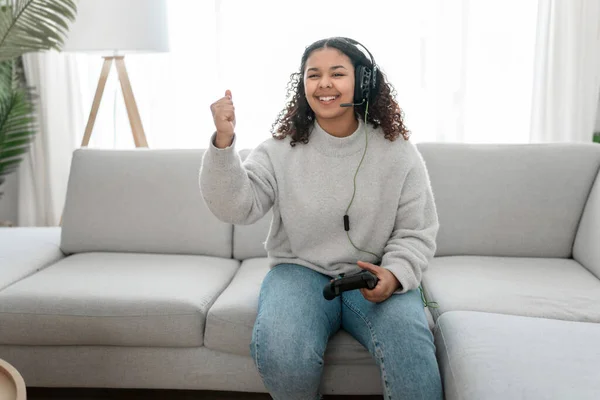 Nuori tummahiuksinen nainen valkoisissa vaatteissa pelaa videopelejä olohuoneessa — kuvapankkivalokuva