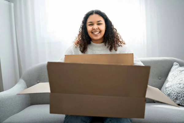 Opgewonden jonge vrouw uitpakken enorme kartonnen doos zitten op de bank thuis — Stockfoto