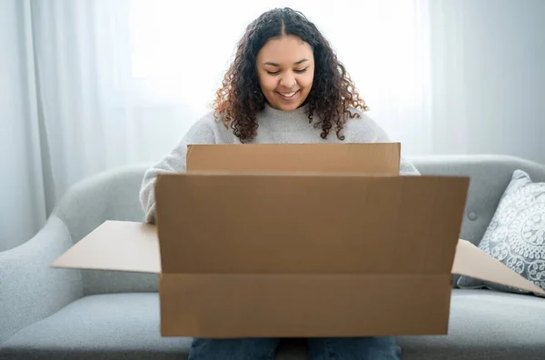 Opgewonden jonge vrouw uitpakken enorme kartonnen doos zitten op de bank thuis — Stockfoto