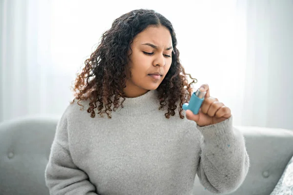 Mujer negra tomando su inhalador en casa en la sala de estar —  Fotos de Stock