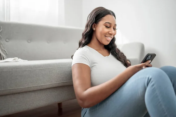 Attraktiv Ung Afrikansk Kvinna Sitter Soffan Hemma Med Mobiltelefon — Stockfoto