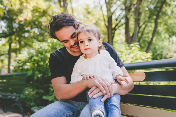 Handsome young father looking at his cute daughter sit on bench — Stock Photo, Image