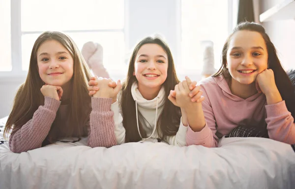 Three excited teenager girls having fun together enjoying laze leisure time on bed — Fotografia de Stock