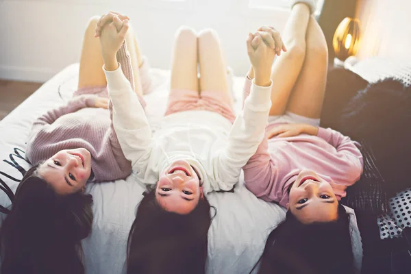 Three excited teenager girls having fun together enjoying laze leisure time on bed — стоковое фото