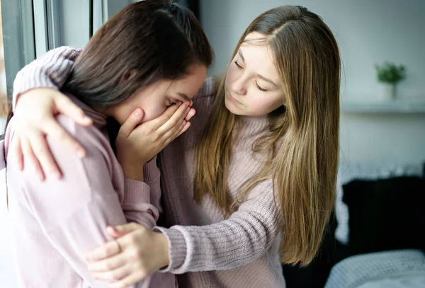 Teenage girl consoling her sad friend on her bedroom — стоковое фото