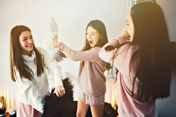 Three excited teenager girls having fun together enjoying laze leisure time with pillow fight — Photo