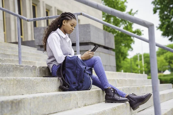 Söt svart tonåring universitetsstudent på campus med ryggsäck och mobiltelefon — Stockfoto