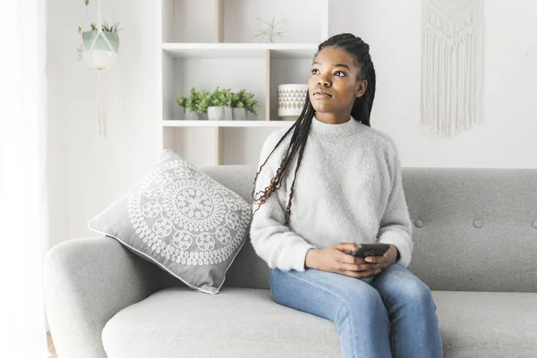 Ung afroamerikansk tonåring på en soffa i hennes vardagsrum med mobiltelefon — Stockfoto