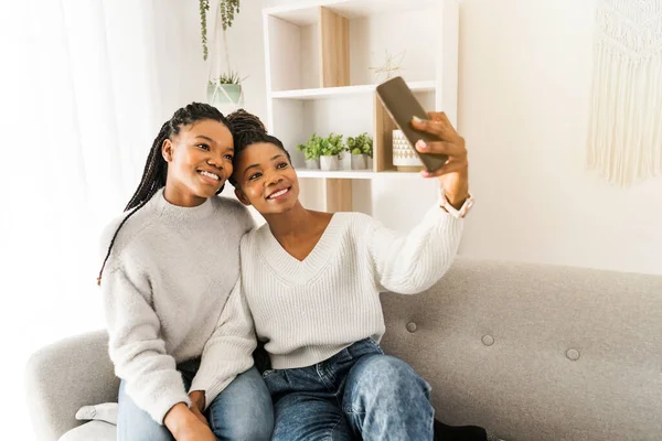 Mother and daughter sitting on sofa at home taking selfie with cellphone — Stockfoto