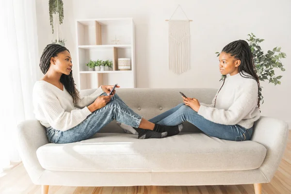 Mother and daughter sitting on sofa at home both using cellphone — Stockfoto