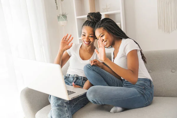 Mother and daughter sitting on sofa at home with laptop talking with family member and say hi — Stockfoto