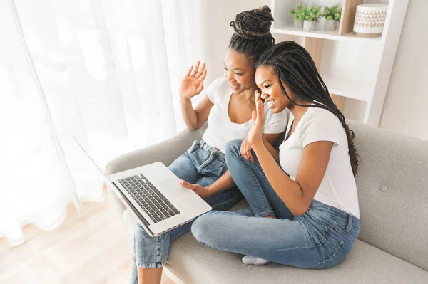 Mother and daughter sitting on sofa at home with laptop talking with family member and say hi — Stockfoto