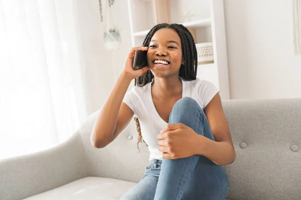 Young African American teen on a sofa in her living room using cellphone — Stockfoto