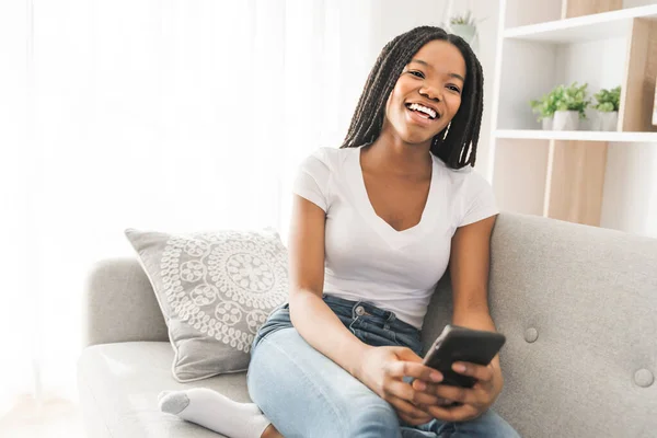 Ung afroamerikansk tonåring på en soffa i hennes vardagsrum med mobiltelefon — Stockfoto