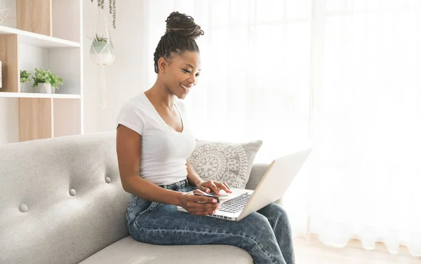 Portrait d'une femme africaine assise sur le canapé à la maison en utilisant un ordinateur portable — Photo