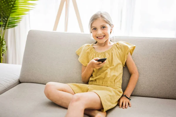 Young girl child sitting on the couch using a remote control — ストック写真