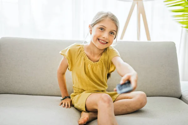 Young girl child sitting on the couch using a remote control — ストック写真