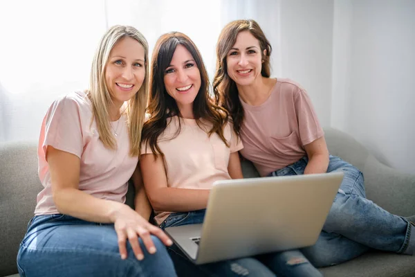 Glimlachen beste meisje vrienden blond en brunette zitten op de bank met laptop — Stockfoto