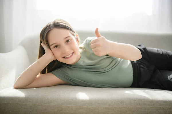 Beautiful pre teen girl relaxing on the sofa at home with thumb up — Fotografia de Stock