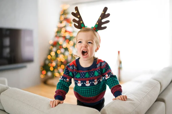 Baby girl with reindeer on head on sofa — Zdjęcie stockowe