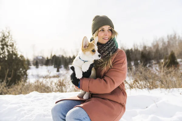 Young happy woman having fun in snowy winter park with Corgi baby dog — стоковое фото