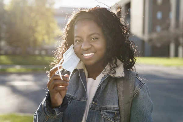 Happy university student taking off her protective face mask outside — Stockfoto