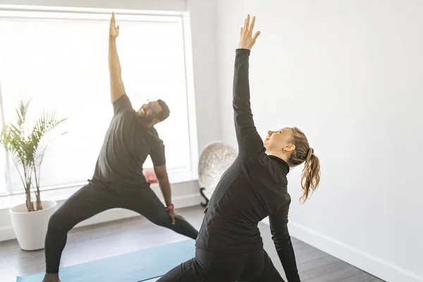 Personal trainer doing yoga pose in sunny studio with client — стоковое фото