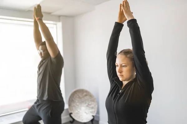 Personal trainer doing yoga pose in sunny studio with client — стоковое фото