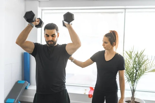 Trainer and client training with dumbbell at the gym — Stockfoto