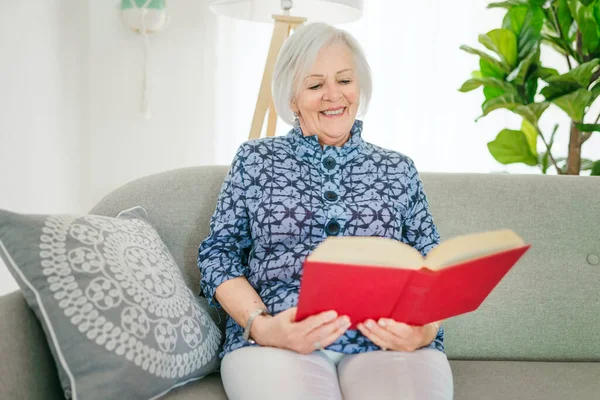 Retrato de anciana sentada en el sofá en casa leer libro — Foto de Stock