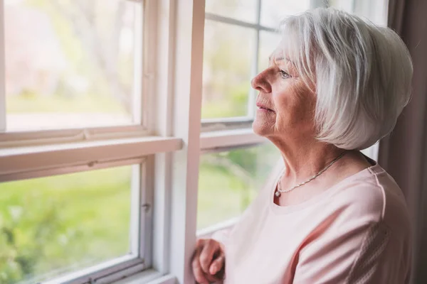Жінка середнього віку перед шторами поруч з вікном відчуває себе самотньою — стокове фото