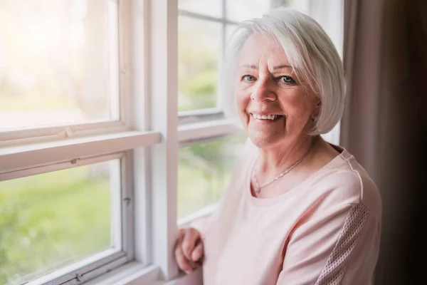 Middle aged female in front of curtains close to a window — Stok fotoğraf