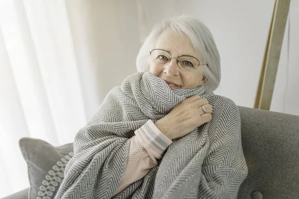 Portrait of elderly woman sit on the sofa at home with warm clothe — Stok fotoğraf