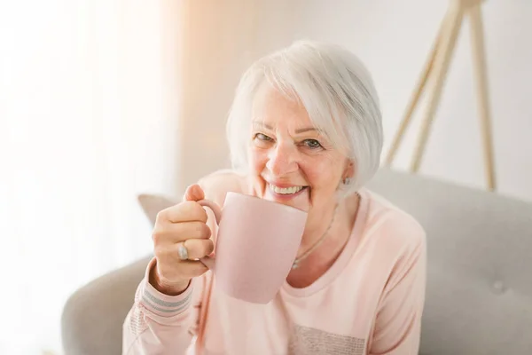 Portrait of elderly woman sit on the sofa at home with coffee or tee — Stok fotoğraf