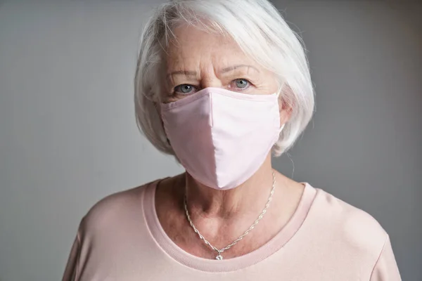 Nice portrait of a retired senior woman on studio background wearing pink covid mask —  Fotos de Stock