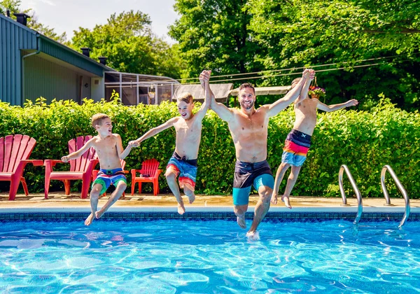 Father and sons having fun jumping on swimming pool — Stock fotografie