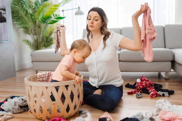 Woman have problem choosing clothes with baby in the living room — стоковое фото
