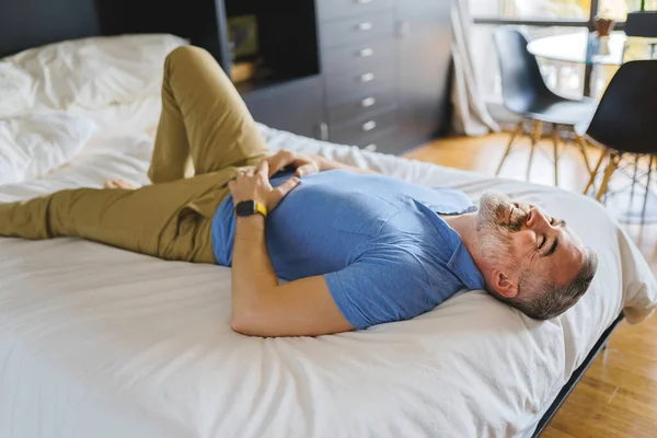 Trevlig mogen man hemma lägenhet med grått skägg avkopplande på sängen — Stockfoto