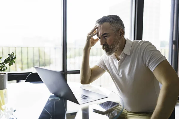 Businessman sitting at desk in bright office using laptop with sad attitude — Foto de Stock