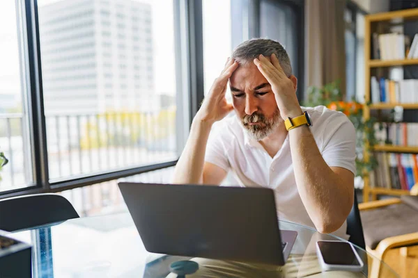 Businessman sitting at desk in bright office using laptop with sad attitude — Foto de Stock