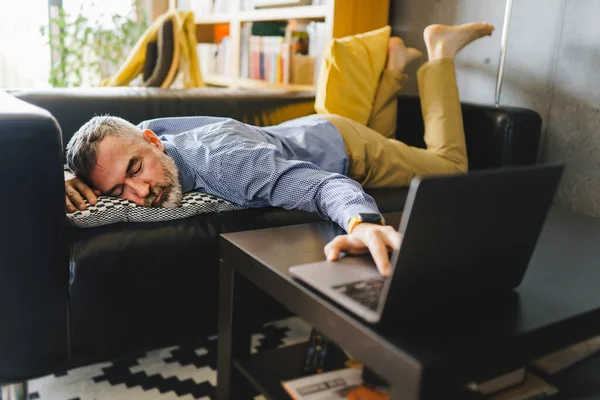 Mature man feeling stress and tired of the computer lay on the couch with a laptop in front — Stock Photo, Image