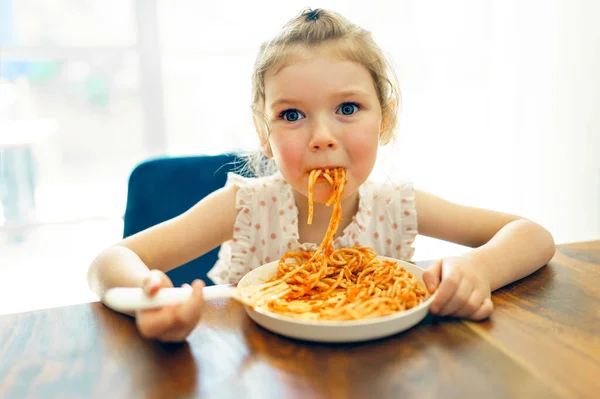 Hungry little girl eating spaghetti at home kitchen — Stockfoto