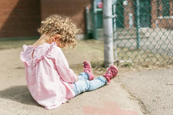 小女孩坐在学校操场上的地板上 — 图库照片