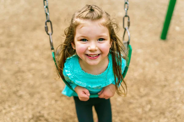 Happy little girl is playground having fun on swing — Stock fotografie