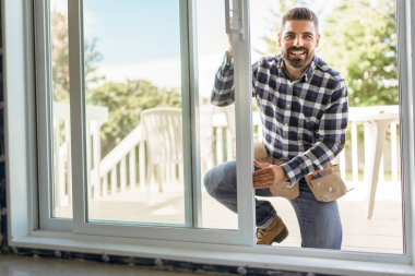handsome young man installing bay window in a new house construction site clipart