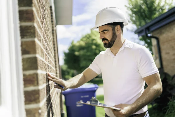 man with a white hard hat holding a clipboard, inspect house