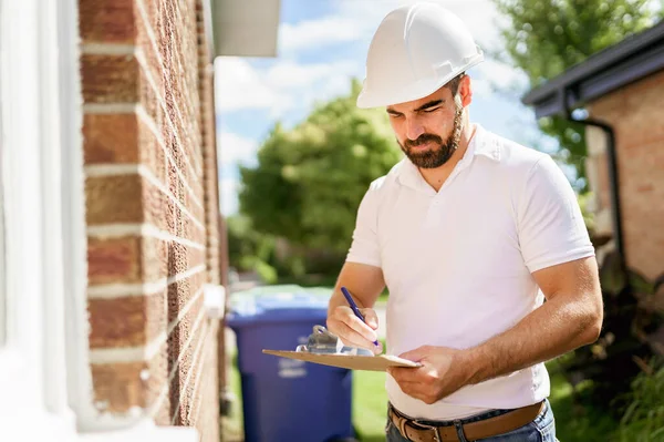 Mann mit weißem Hut hält Klemmbrett in der Hand, inspiziert Haus — Stockfoto