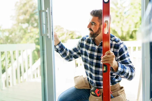 Handsome young man installing bay window in a new house construction site with level — Stockfoto