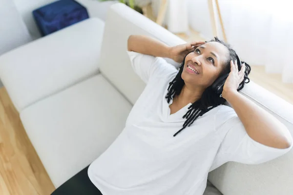 Kvinna med hörlurar på soffan och lyssna på musik — Stockfoto