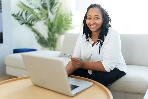 Φωτογραφία της όμορφης μαύρης γυναίκας που χρησιμοποιεί φορητό υπολογιστή στο σπίτι καναπέ και να αγοράσει κάτι στο διαδίκτυο — Φωτογραφία Αρχείου